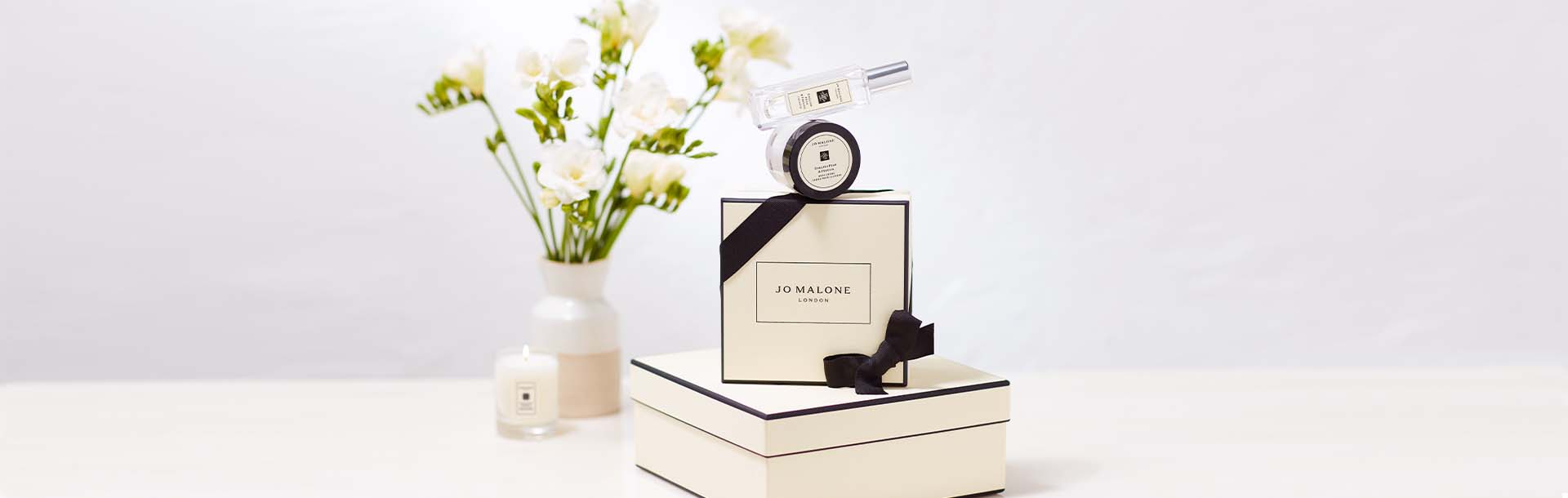 iconic jo malone london black & cream gift boxes stacked with a vase of flowers, travel candle & body creme